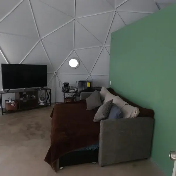 Interior del domo en Las Águilas con sofá, cama y pared verde, ilustrando el amueblado minimalista