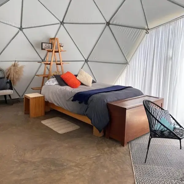 Interior del domo en Los Cedros con cama, textiles neutros y repisas de madera, creando un ambiente minimalista y acogedor