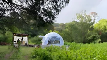 Vista panorámica del domo geodésico de Glamping Los Cedros rodeado de vegetación y su área de atención al fondo